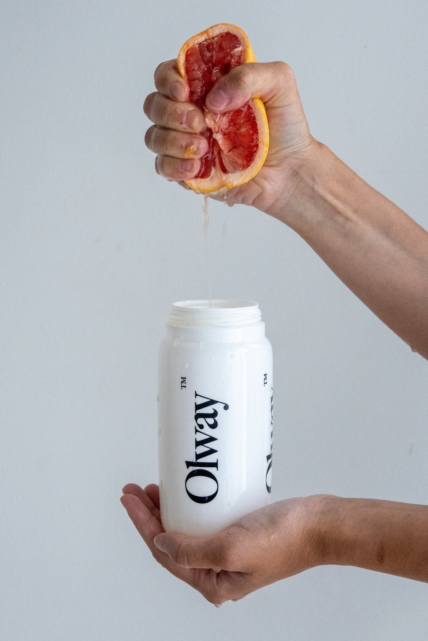 Hand squeezing fresh grapefruit into Olway Performance Drink Mix for a custom-flavoured, unflavoured endurance hydration drink