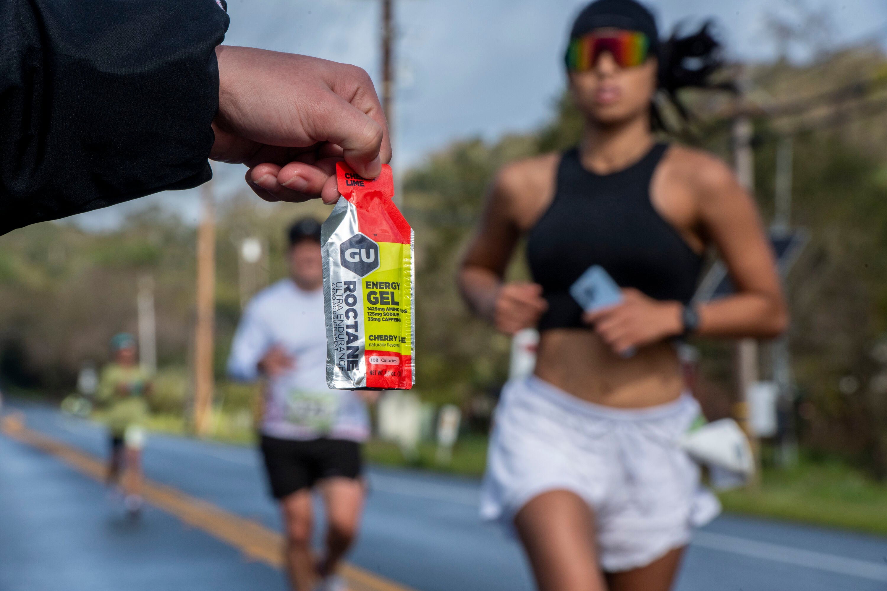 Picture of a person holding out a Gu energy gel for runners in a race