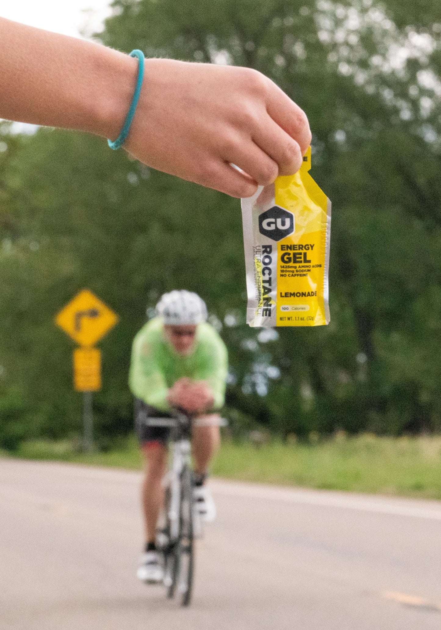 Person holding Lemonade Gu Energy Gel out for a cyclist