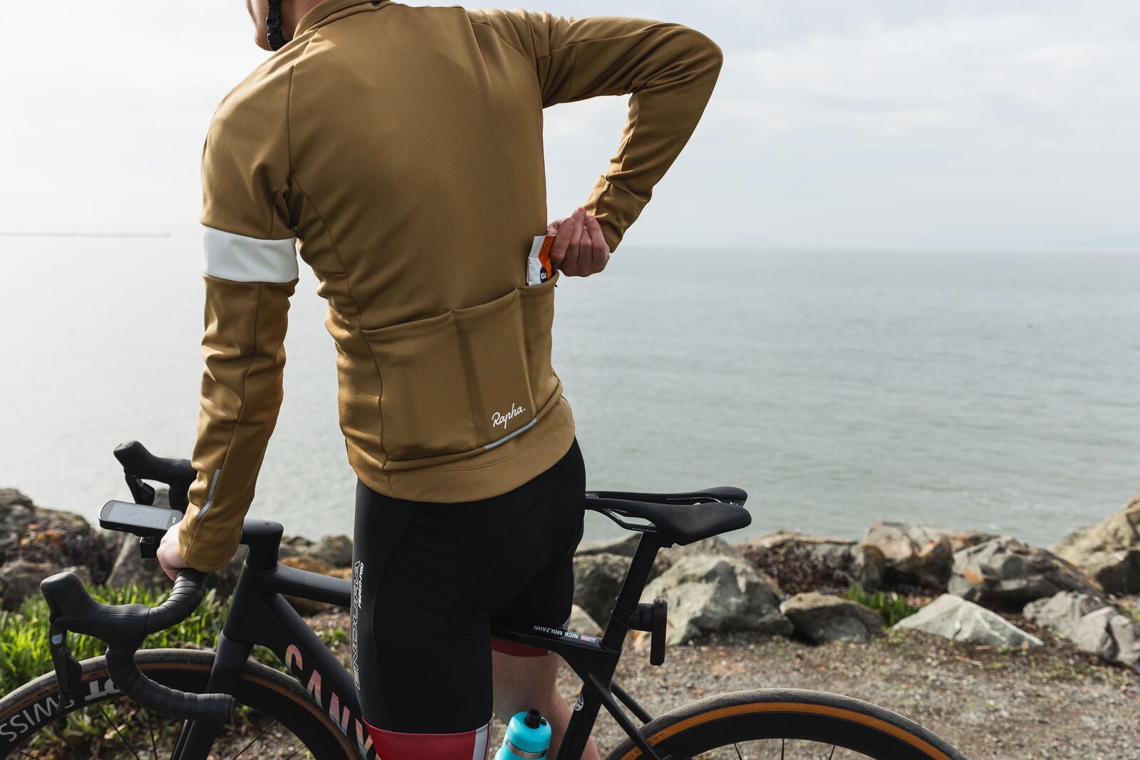 Picture of a cyclist by the ocean putting Gu Chews into his cycling shirt