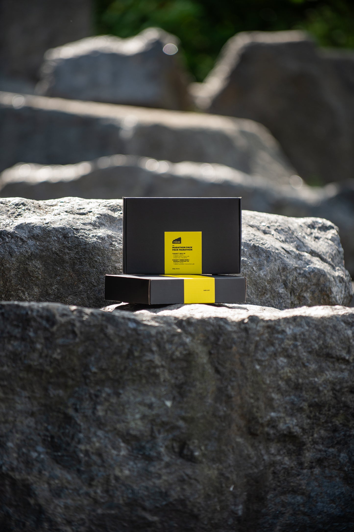Two black naak Marathon Pack boxes with bright yellow labels are placed on large gray rocks outdoors | Fuel Kit