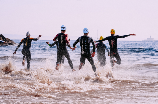 Triathletes running into an ocean with wetsuits on