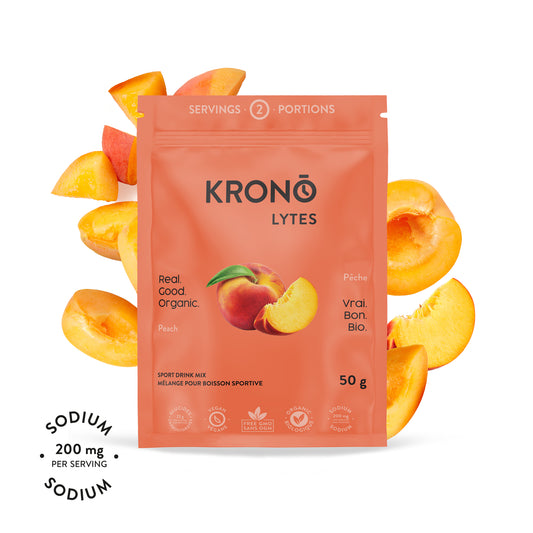 A packet of Krono Nutrition Krono Lytes with peaches around it. The packet indicates the product is organic, vegan, and provides a sodium content of 200 mg per serving.
