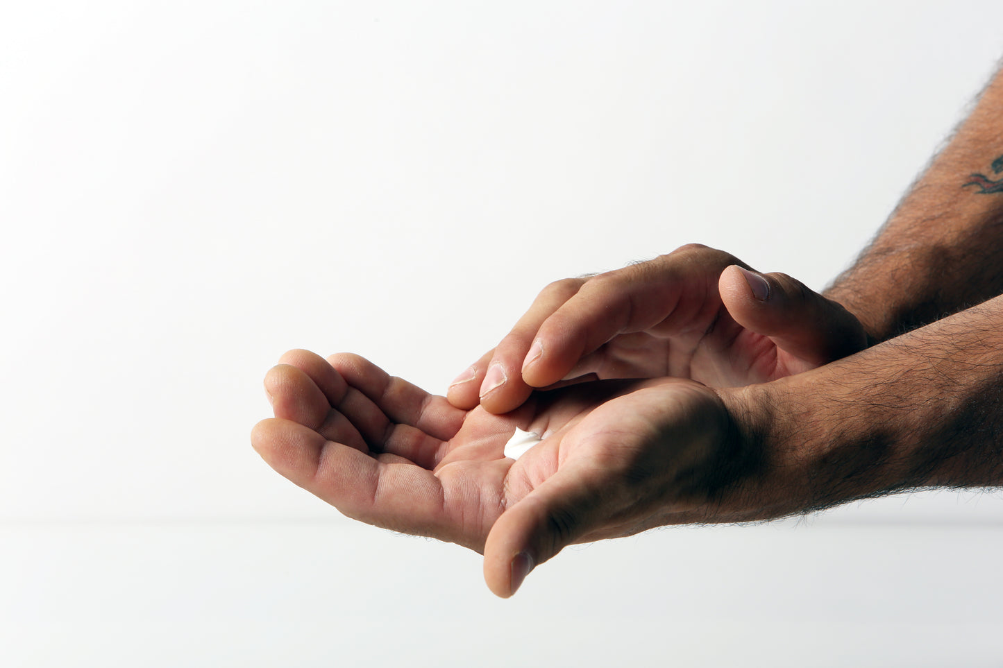 Close-up of a person's hands holding a small amount of FrictionLabs liquid chalk cream before spreading it, available at Fuel Kit.