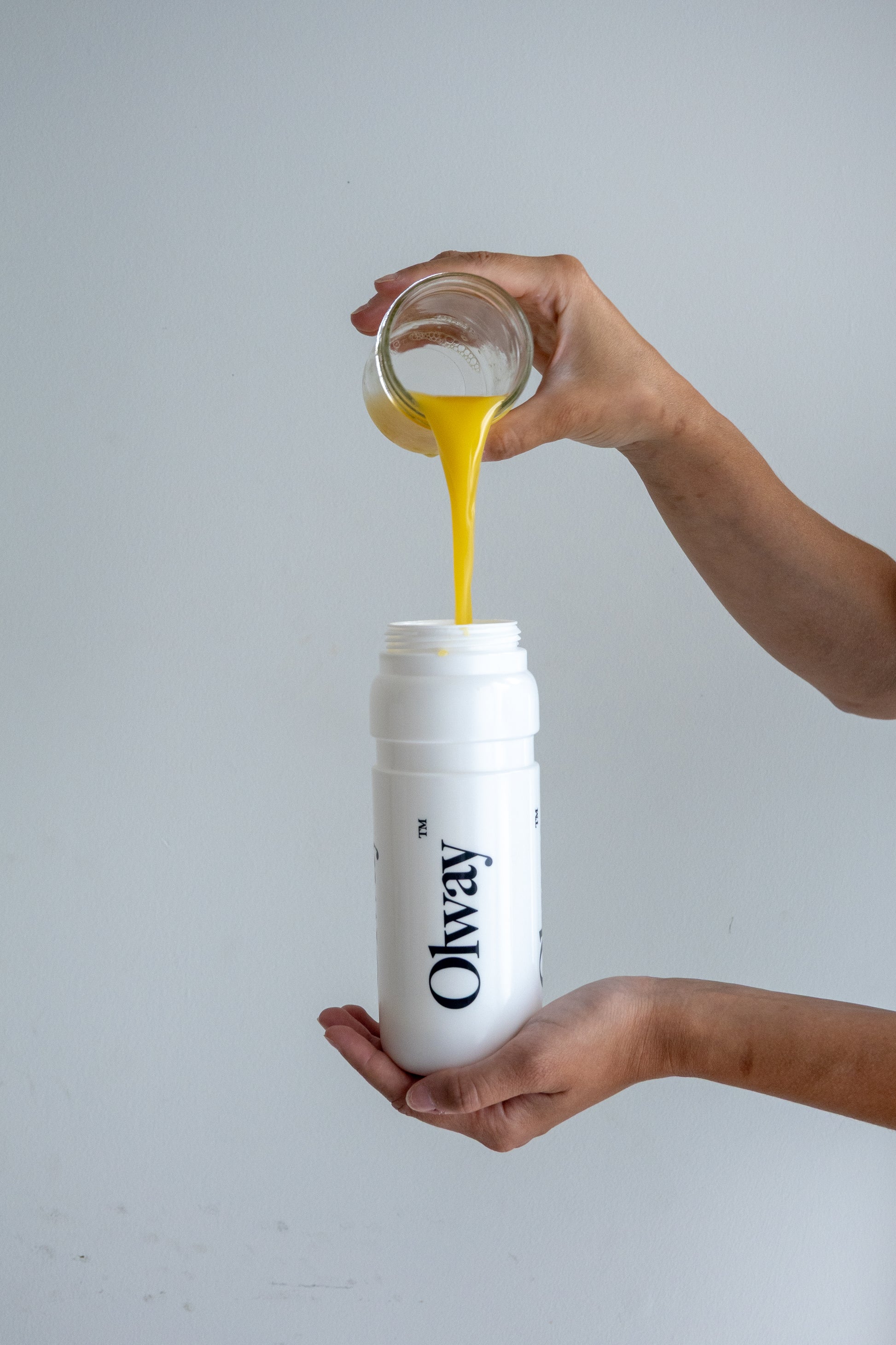 Hand holding an Olway Performance water bottle and pouring orange juice into it to flavour unflavoured drink mix, ready for use in a Fuel Kit