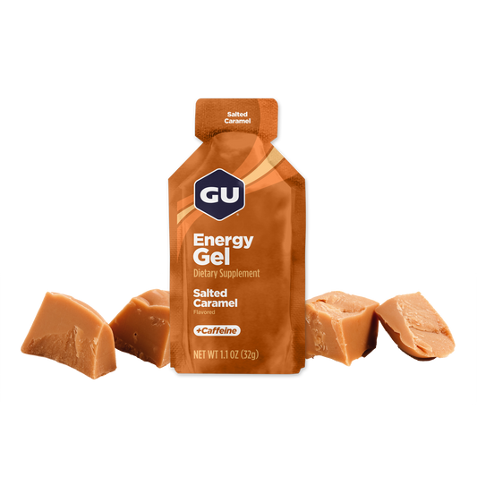 A packet of GU Energy Gel in Salted Caramel flavor, with visible pieces of caramel beside it.