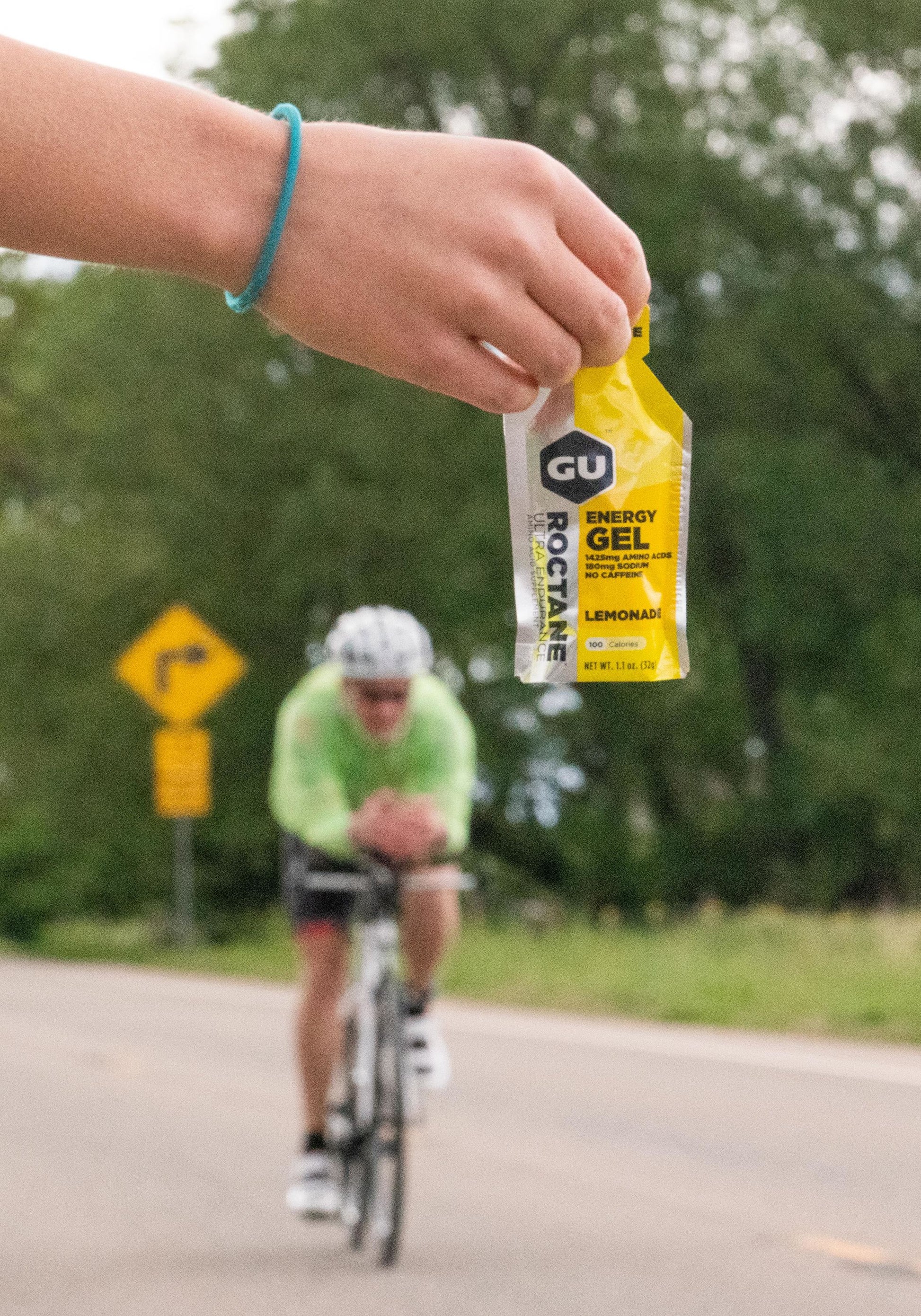 Person holding Lemonade Gu Energy Gel out for a cyclist