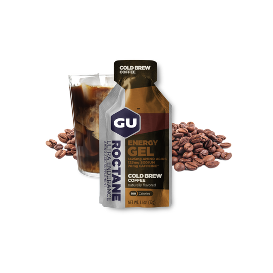 A packet of GU Roctane Energy Gel with a cup of cold brew coffee and coffee beans in the background.