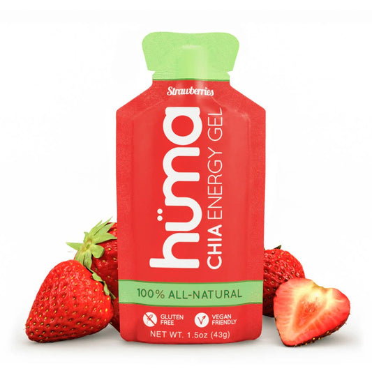 A packet of Huma Plus Gel with a strawberries flavor, alongside strawberries. The gel packet is red with text and branding, indicating it is 100% all-natural.