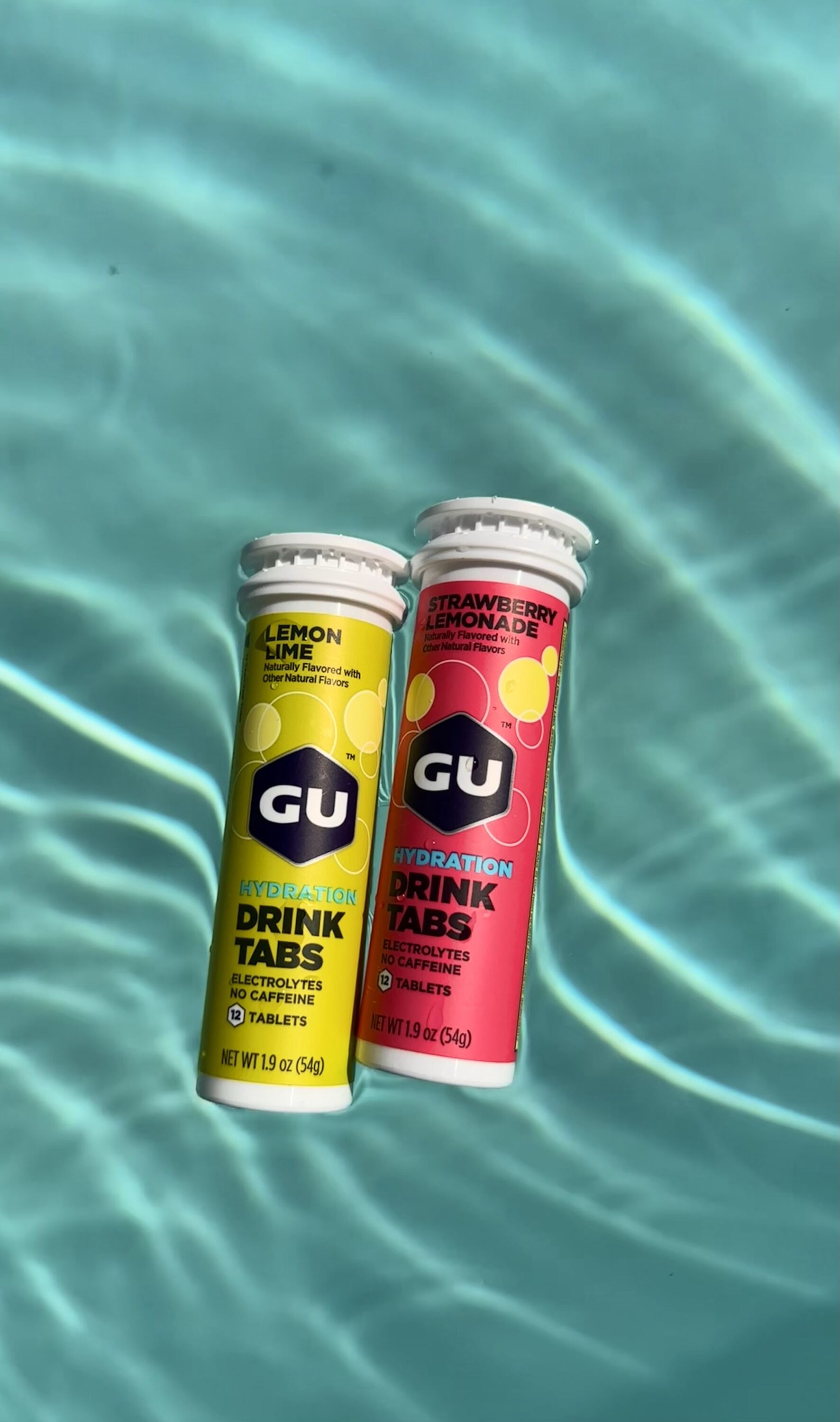 Lemon Lime and Strawberry Lemonade Gu Drink Tab canisters floating in pool water