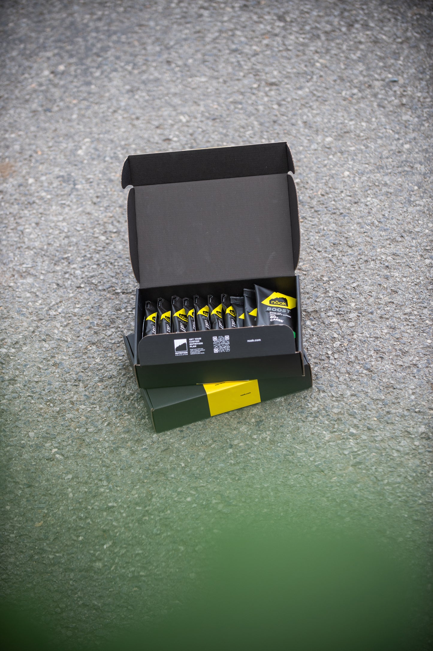 An open naak Marathon Pack box containing multiple small gels and drinks, placed on a textured gray surface outdoors | Fuel Kit