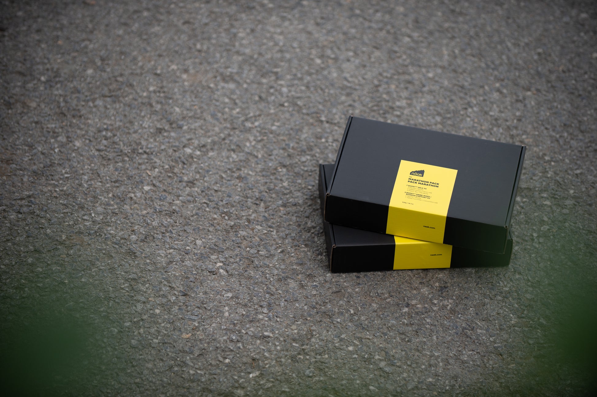 Two black rectangular naak Marathon Pack boxes stacked on a gray asphalt surface, each with a bright yellow label on the front | Fuel Kit