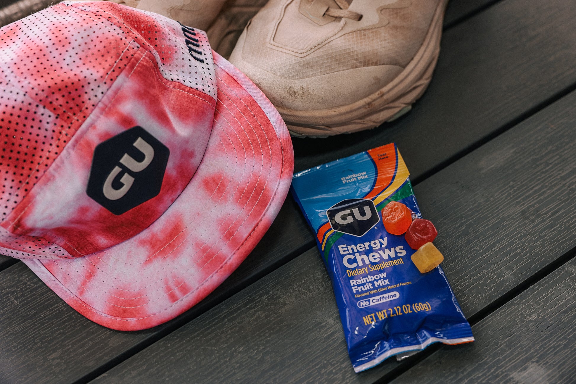 Pink and white cap with black logo, beige shoe, and blue GU Rainbow Fruit Mix Energy Chews packet- Fuel Kit