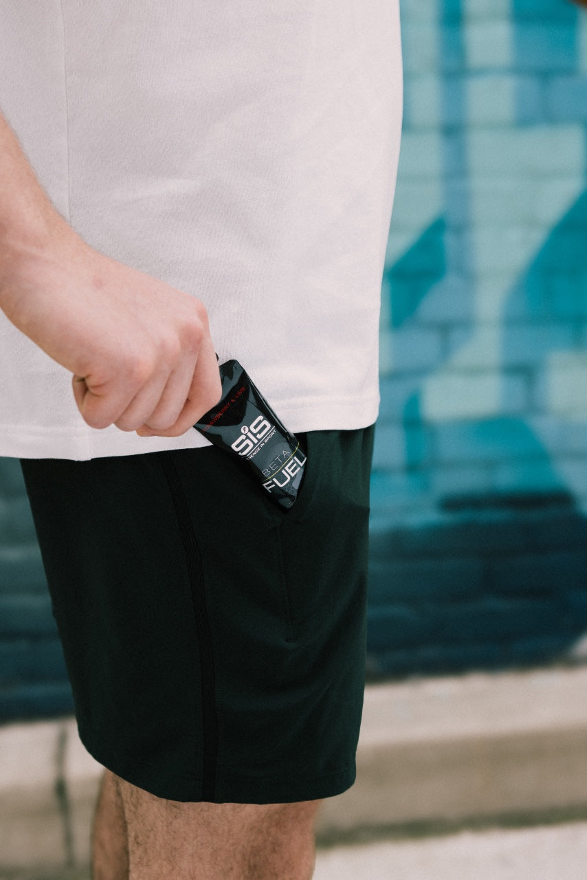 Person holding a black SiS energy gel packet with a blurred background