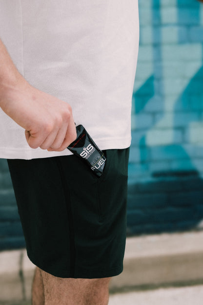 Person holding a black SiS energy gel packet with a blurred background