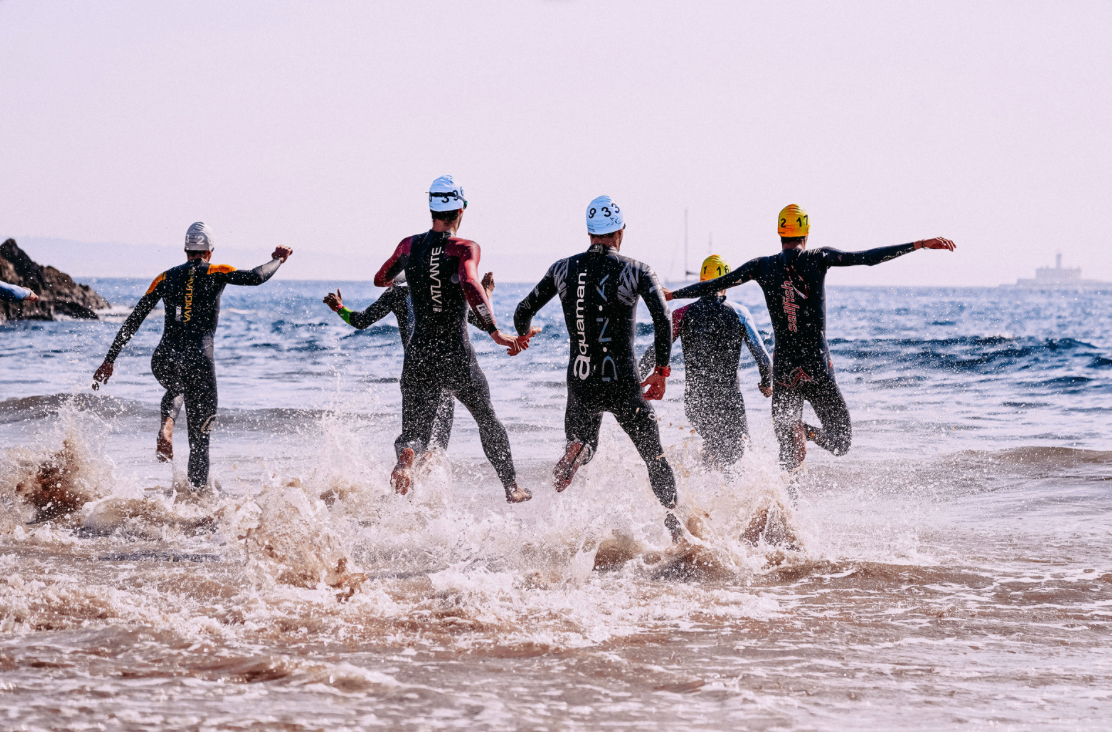 Triathletes in wetsuits running into the ocean, after fueling with Fuel Kit.