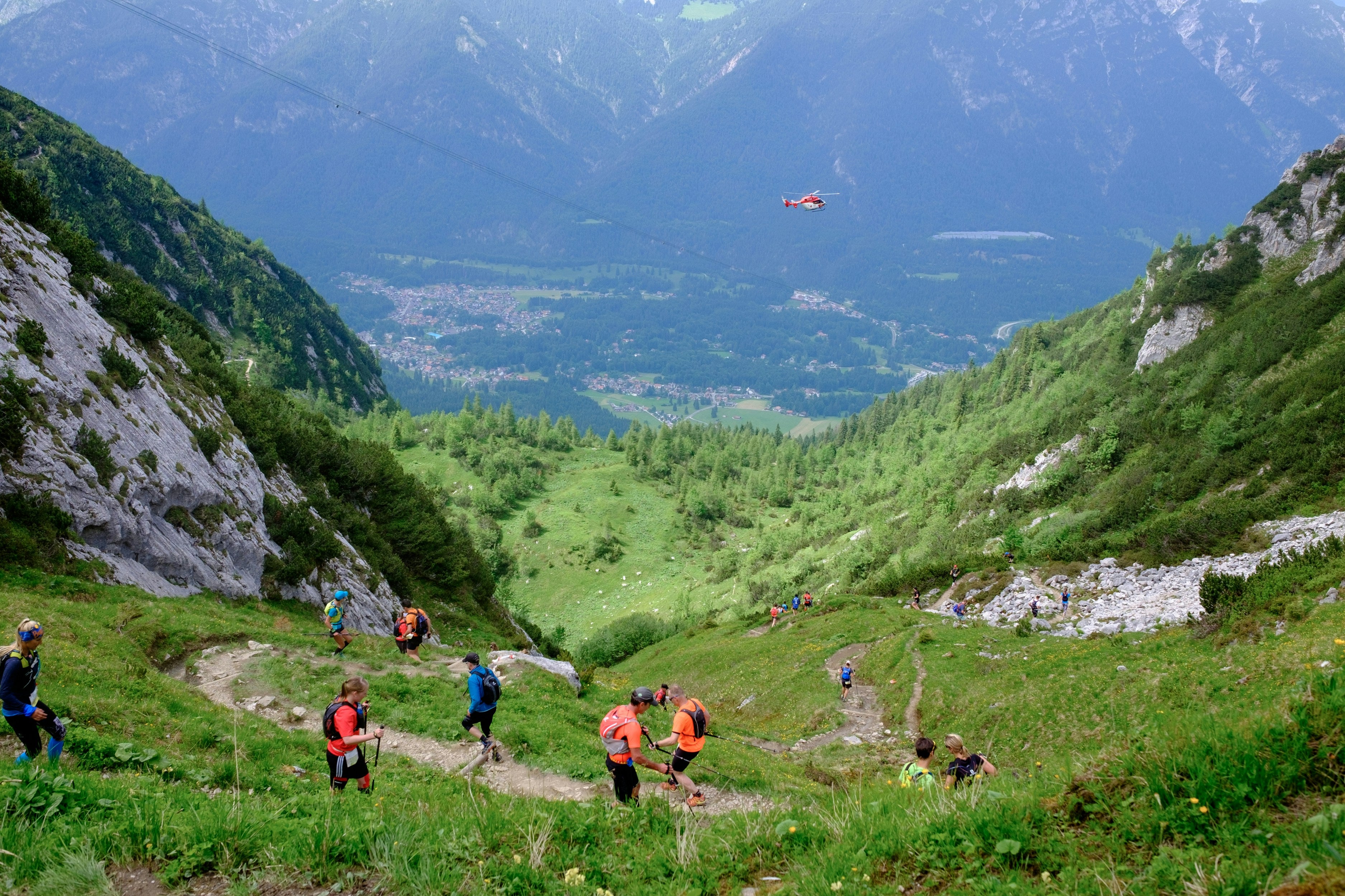 Trail runners on a trail in a mountainous landscape with a helicopter in the distance using their easy nutrition fuel kits to fuel their performance.
