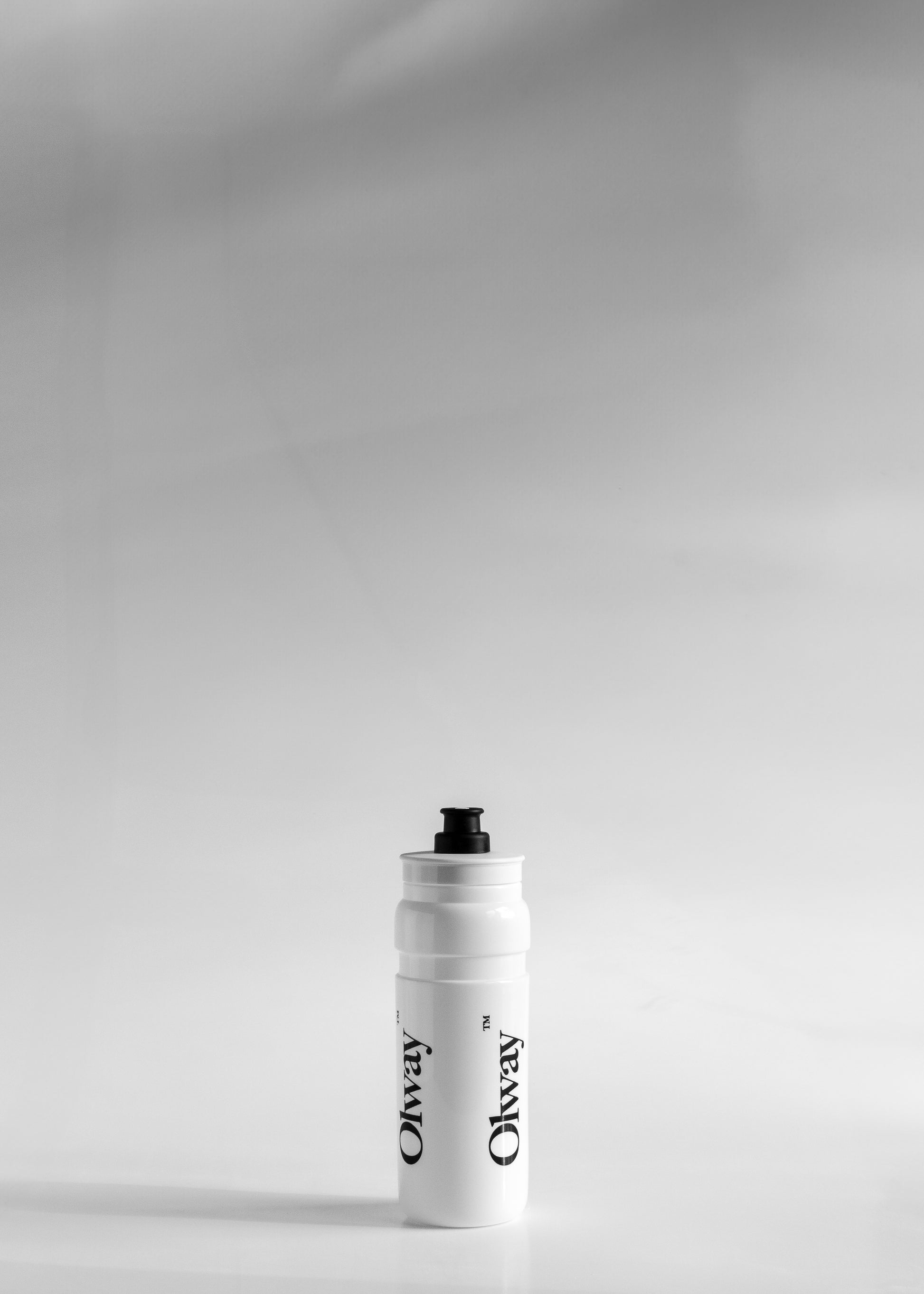 A white Oway water bottle with a black cap, standing upright on a light gray surface available at Fuel Kit.