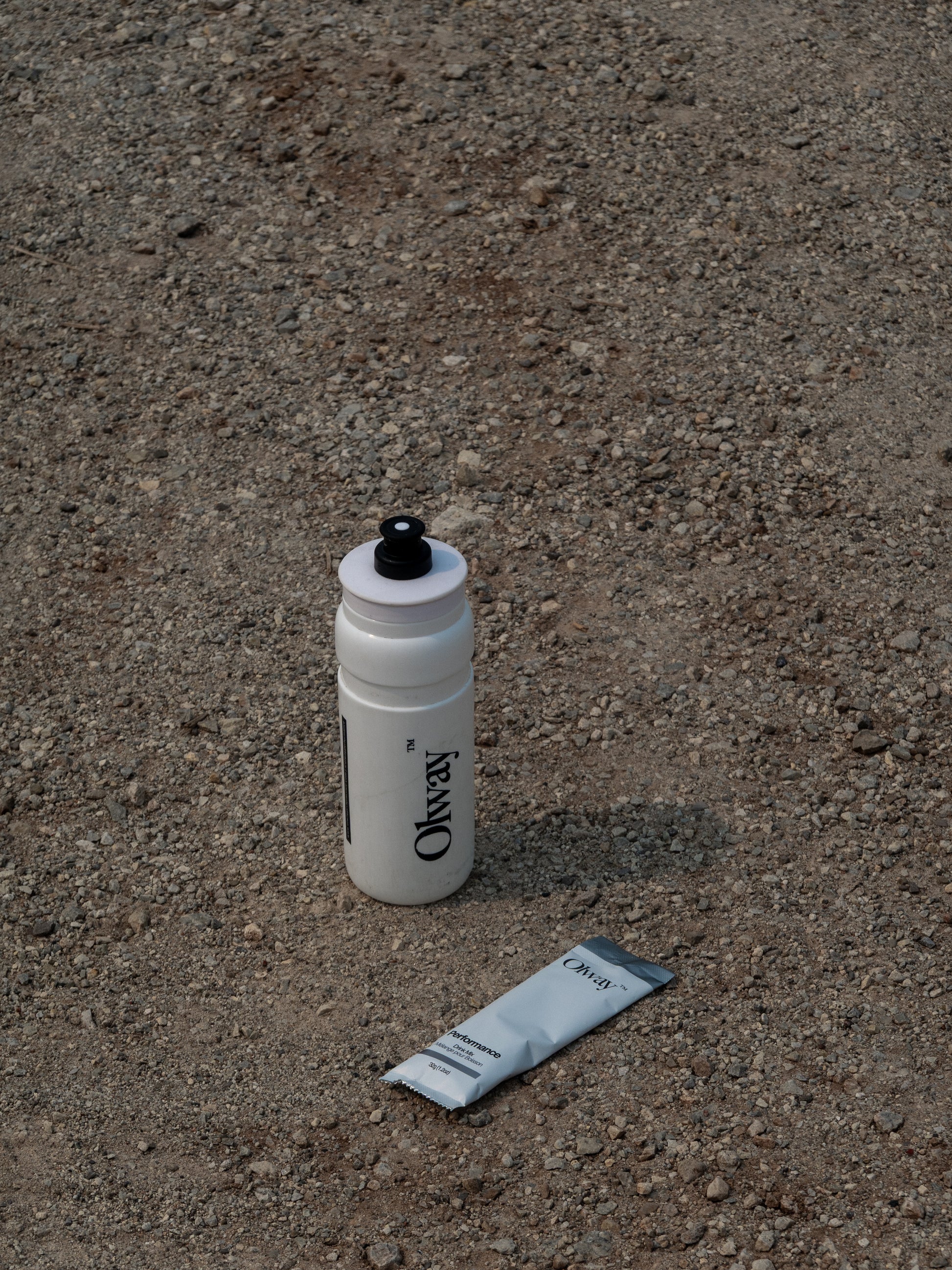 White Olay wtaer bottle on gravel with a packet of Olway Drink Mix, available at Fuel Kit