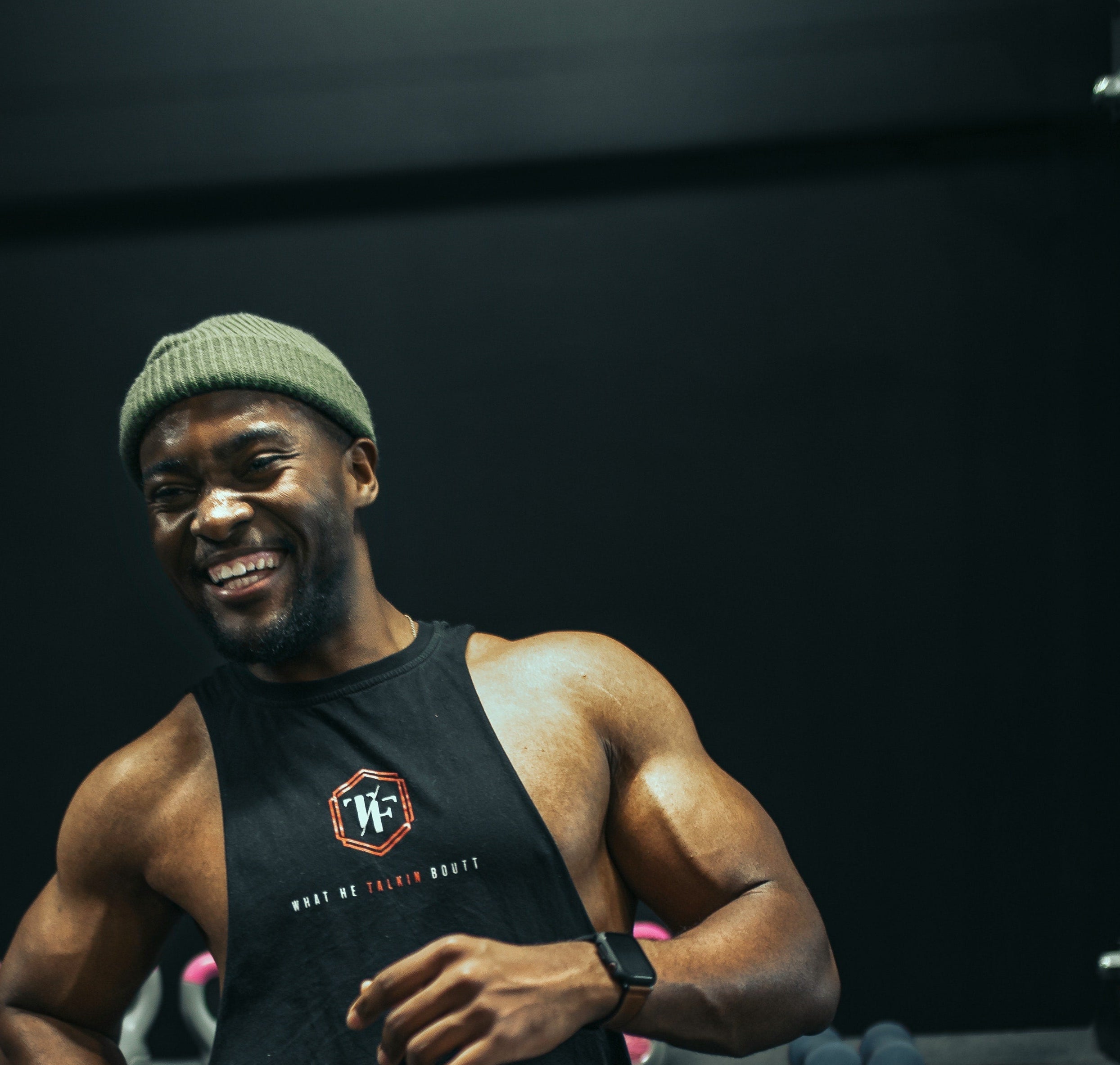 Man competing in HYROX wearing a black tank top with a logo and a green beanie, standing against a dark background needing easy fueling tips from the Fuel Kit blog