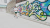 Picture of a runner beside a graffiti wall running and taking a sports gel